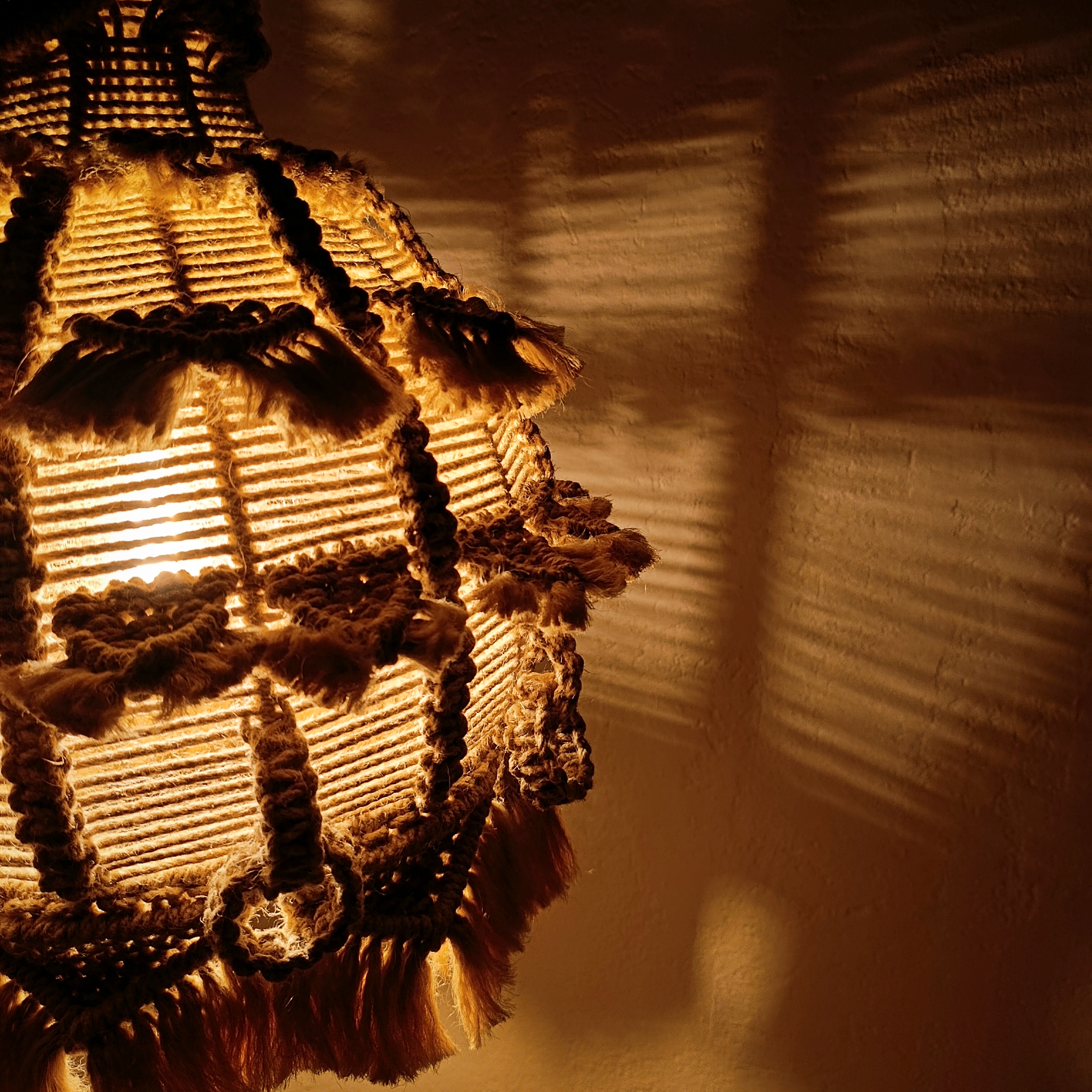 Product photo in detail of La Alma de Barro by Koko Bamboo, it shows the impressive centerpiece lamp illuminated, casting detailed and dappled shade on the wall behind it