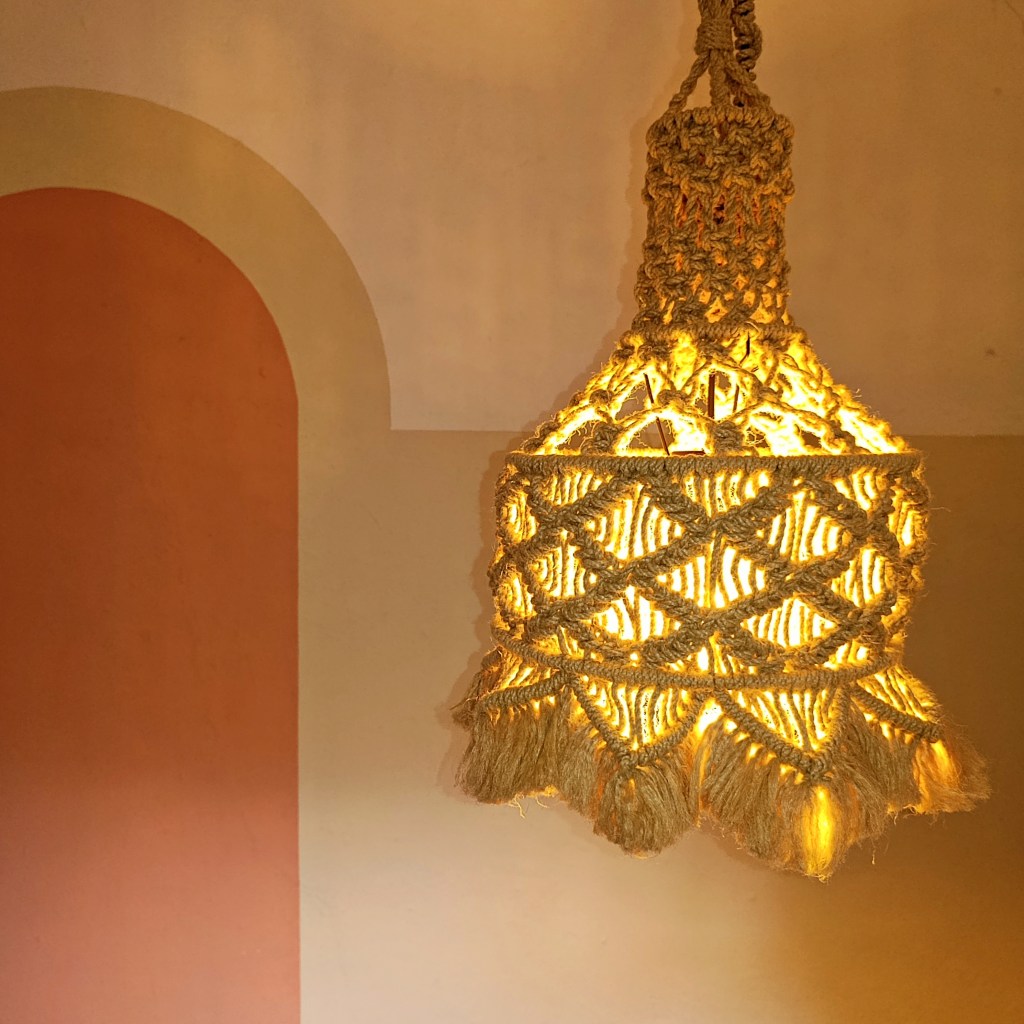 Product shot of La Pluma Dorada by Koko Bamboo, macramé hanglamp in original design in illuminated form inside a painted room